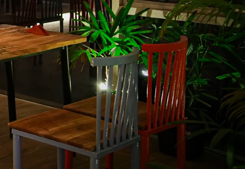 Timber tables with orange and grey chairs, set against dense planting
