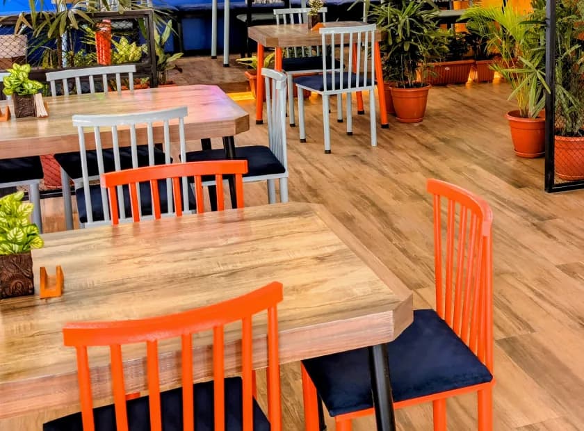 Orange chairs and timber tables on the oak floor, framed by potted greenery